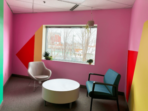 Photograph of a colourful common area with a round table and two seats in front of a window.