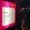 Photograph of Brampton poet Rosie Arulanandam looking at her poem at a bus shelter at Trinity Commons at night.