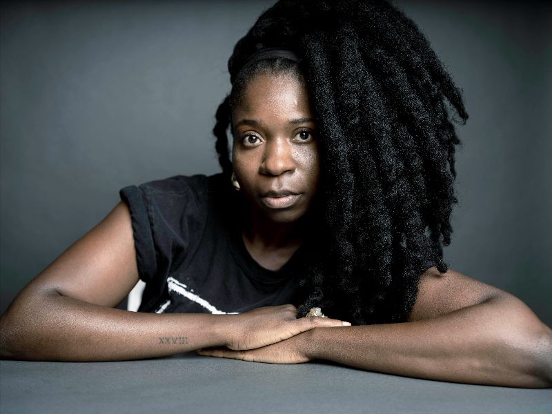 a Young Black woman who is wearing a black t-shirt crossing her arms on a grey table