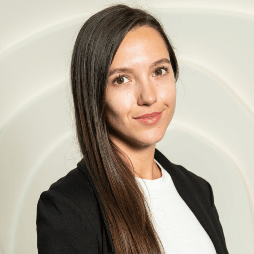 Photograph of a woman with long straight hair. She is wearing a white blouse and a black blazer.