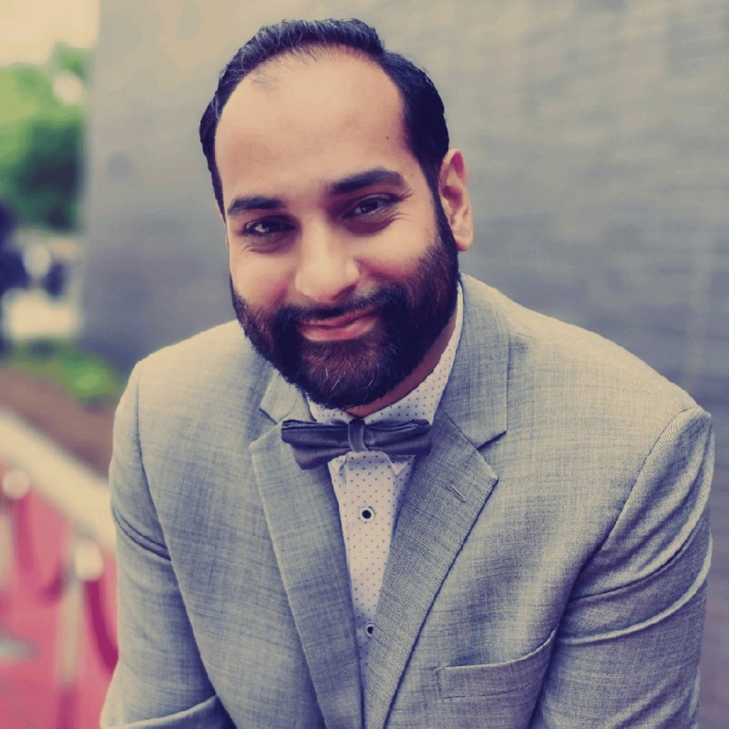 Photograph of a South Asian man with a beard. He is wearing a gray suit, white polka dot shirt and a bowtie.
