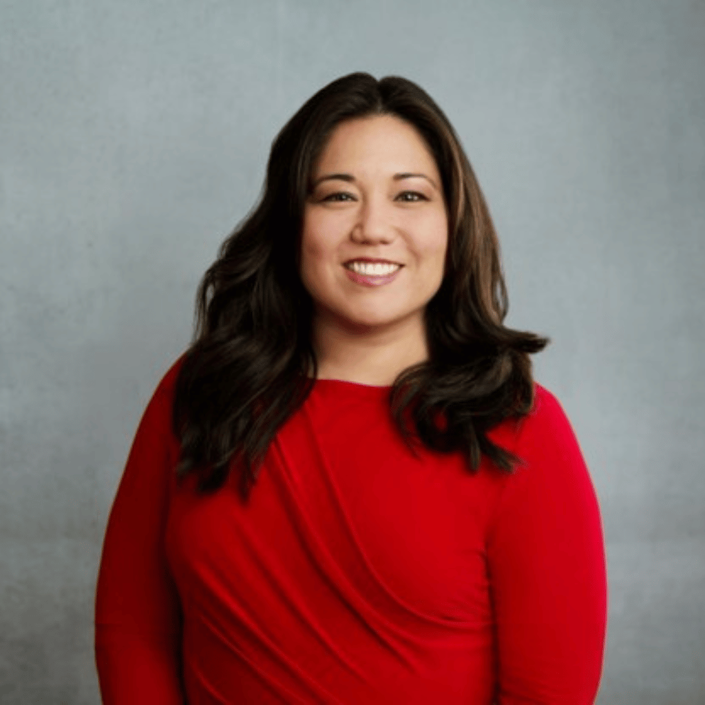 Photograph of an East Asian woman with dark shoulder length hair. She is wearing a red long sleeved blouse.