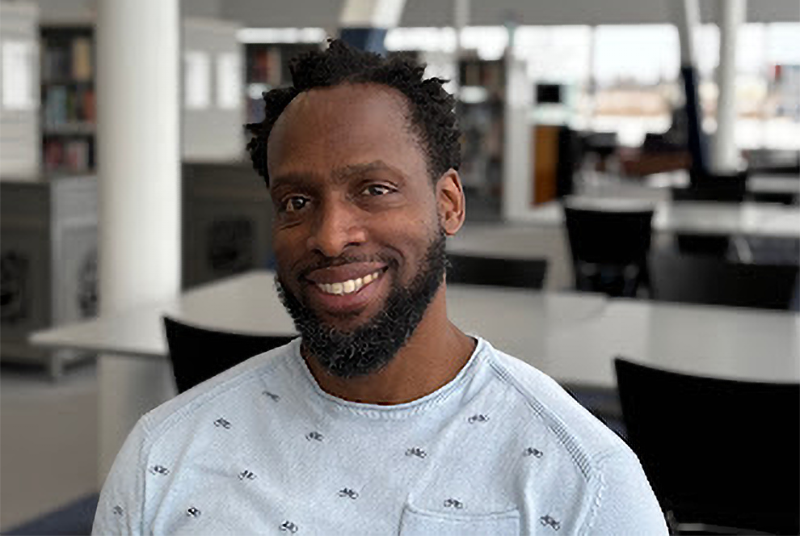 A young Black man wearing a light blue long sleeve shirt in an office