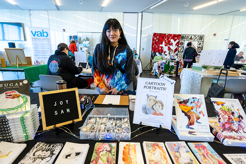 A young asian woman standing in her booth at a winter BAO art market in brampton 