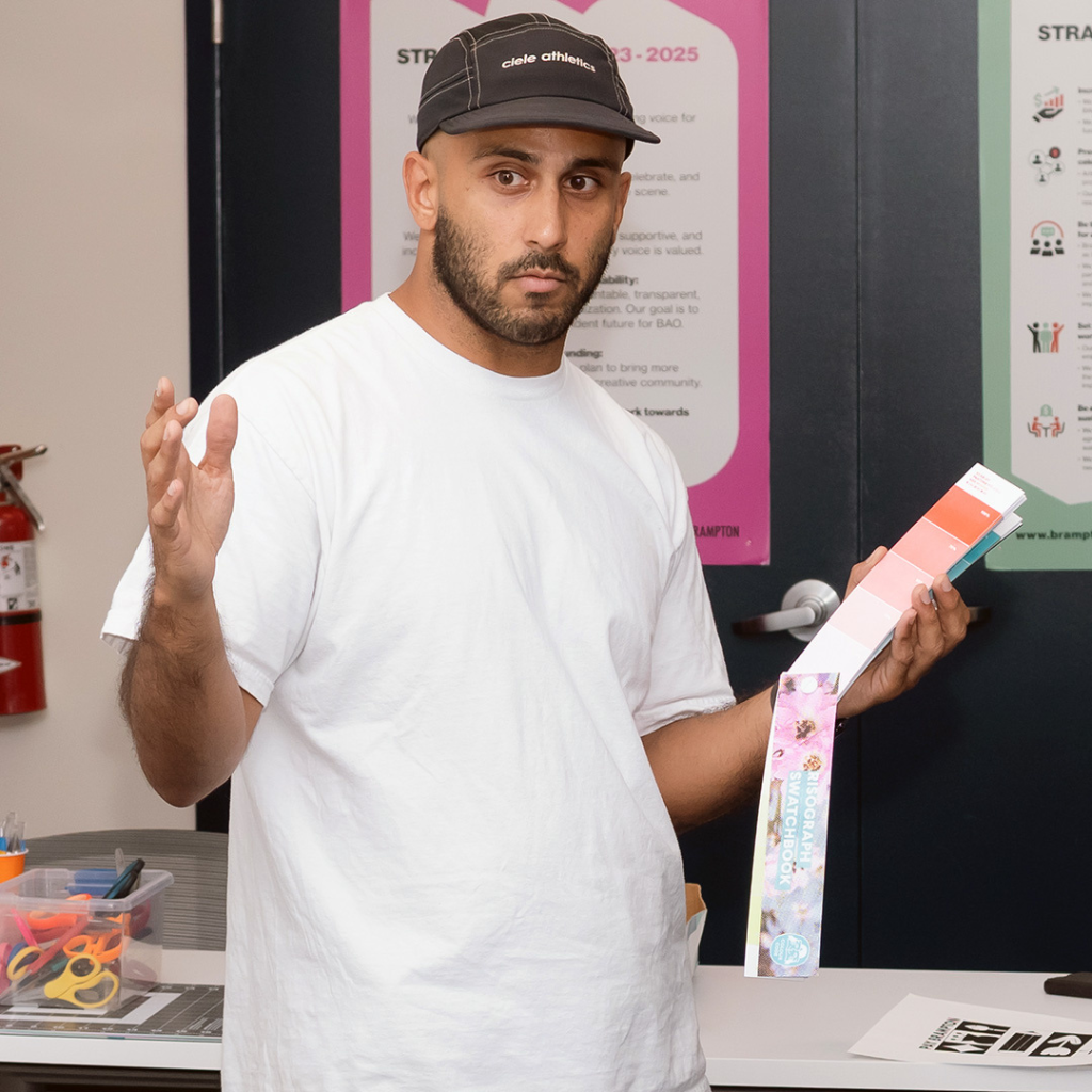 Photograph of Jesjit Gill, a South Asian man with a neatly trimmed beard. He is wearing a white t-shirt and black cap.