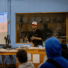 A young Black man is teaching at the front of a classroom