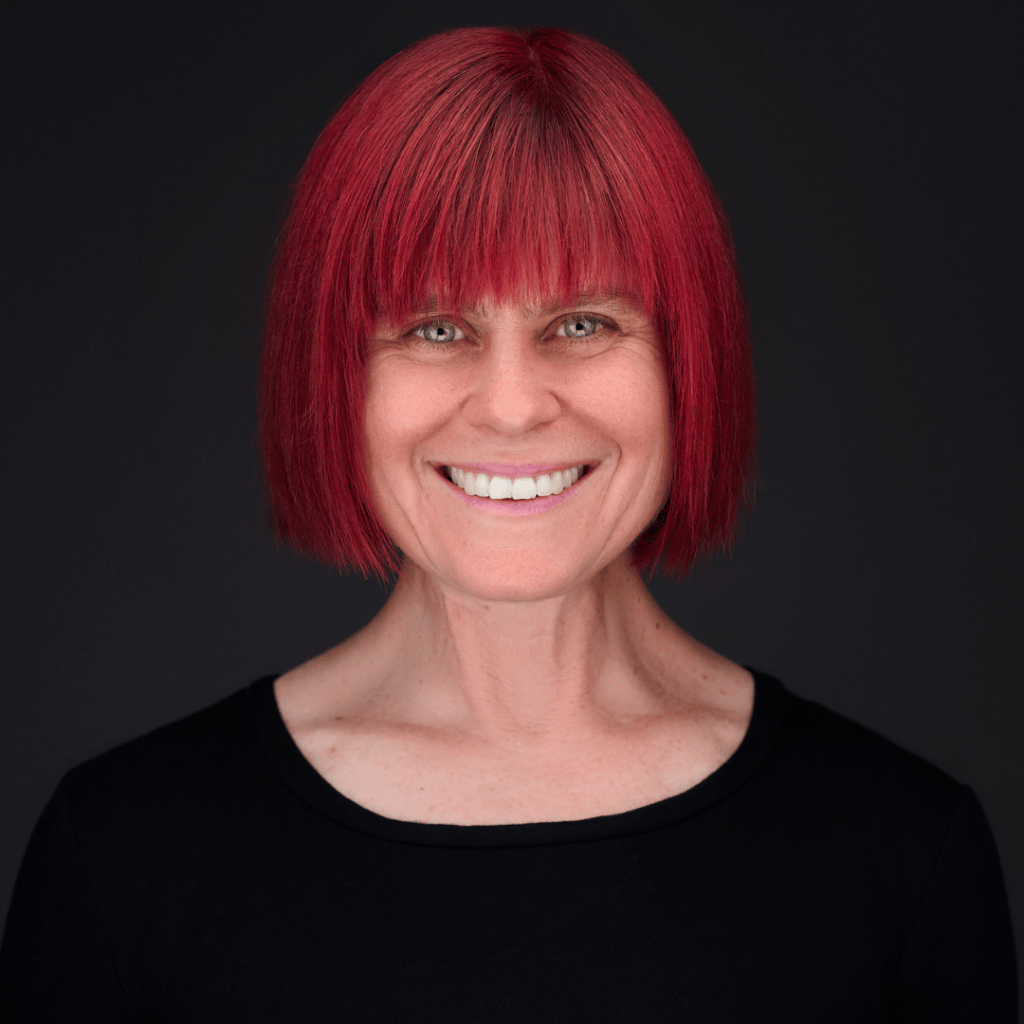 Photograph of Vanessa Burns, a white woman with green eyes and a short red bob. She is wearing a black blouse.