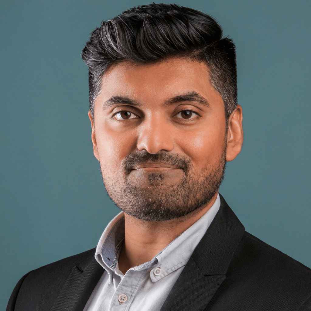 Photograph of Farrukh Rafiq, a South Asian man with short brown hair and a neatly trimmed beard. He is wearing a button-down shirt with a dark blazer over it.