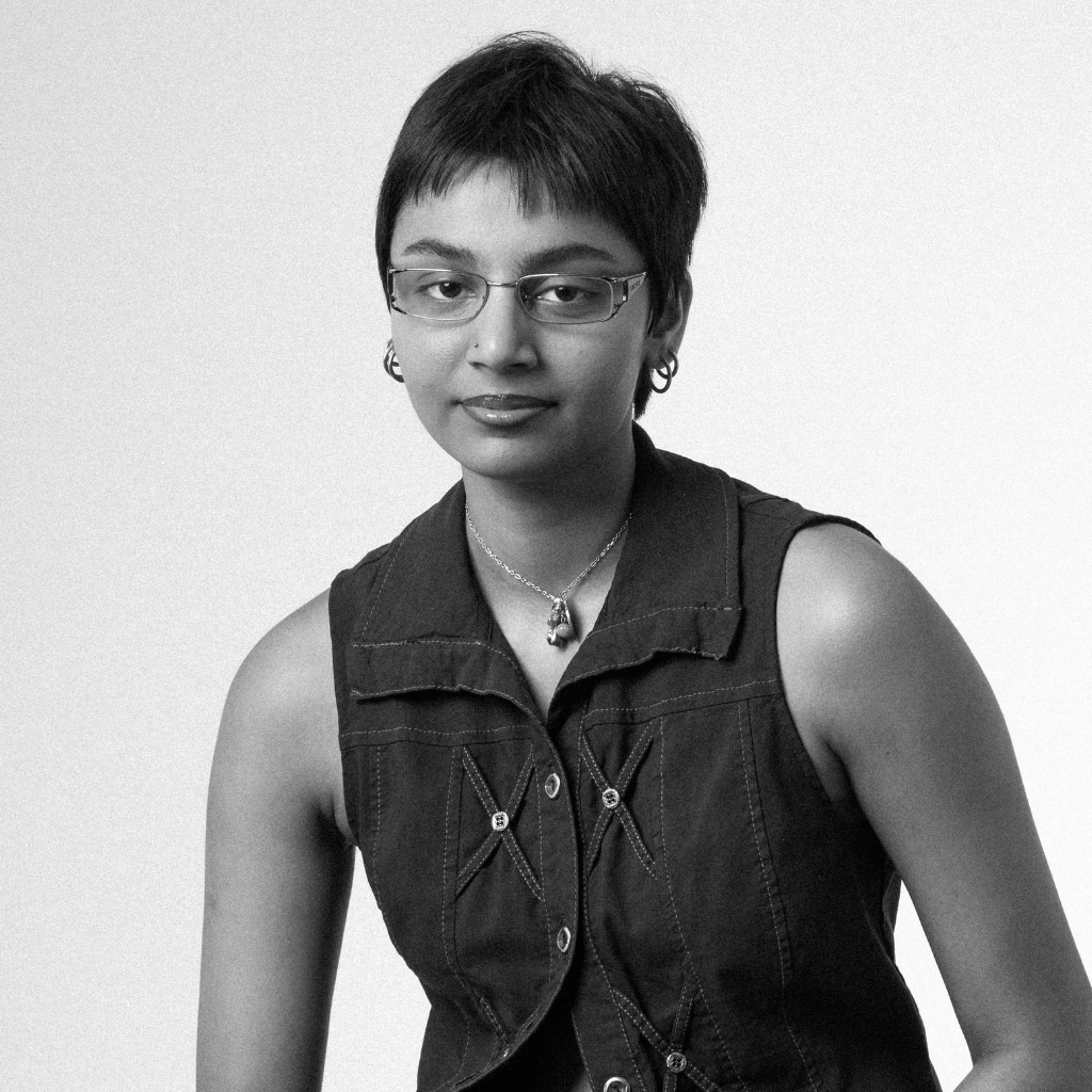 Photograph of gulzar, a South Asian person with short Black hair and wire rimmed glasses. They are wearing a denim vest.