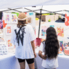 photograph of an adult and child shopping at an artist vendor booth at the 2025 Brampton Farmers' Market